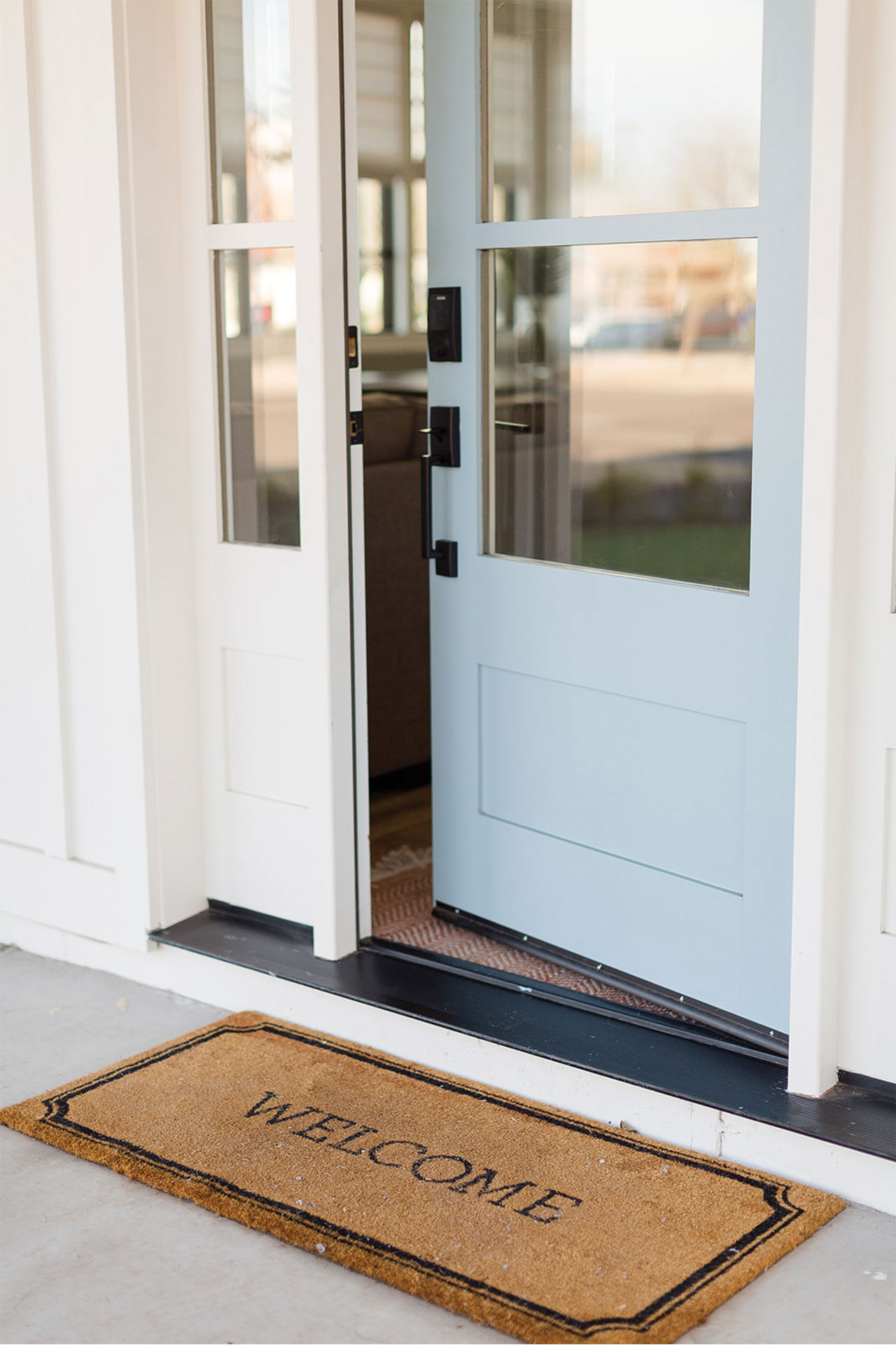 Light Brown Welcome Mat in Front of Opened White Front Door with Windows